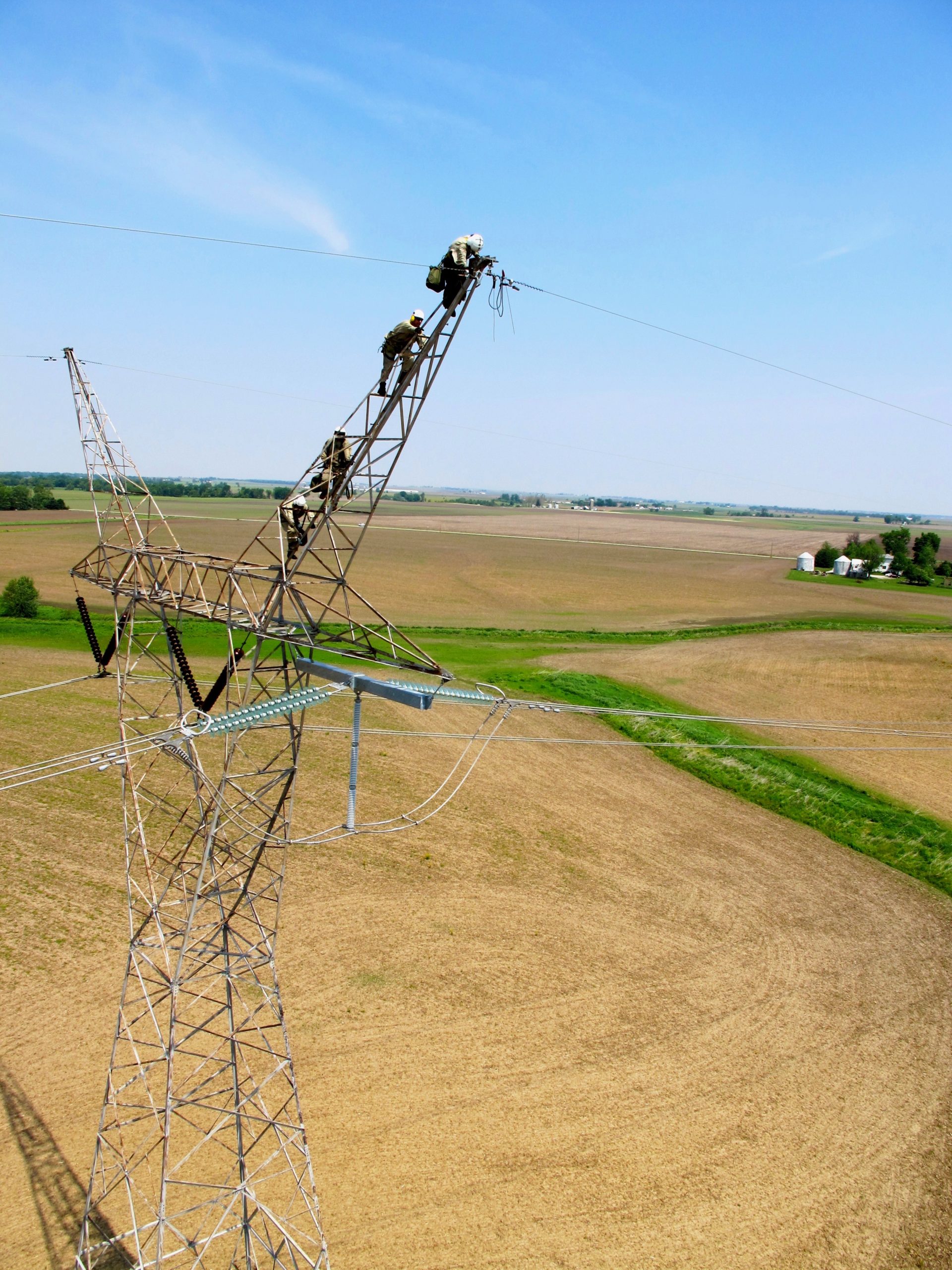 A group of individuals works on electrical lines in a rural setting.