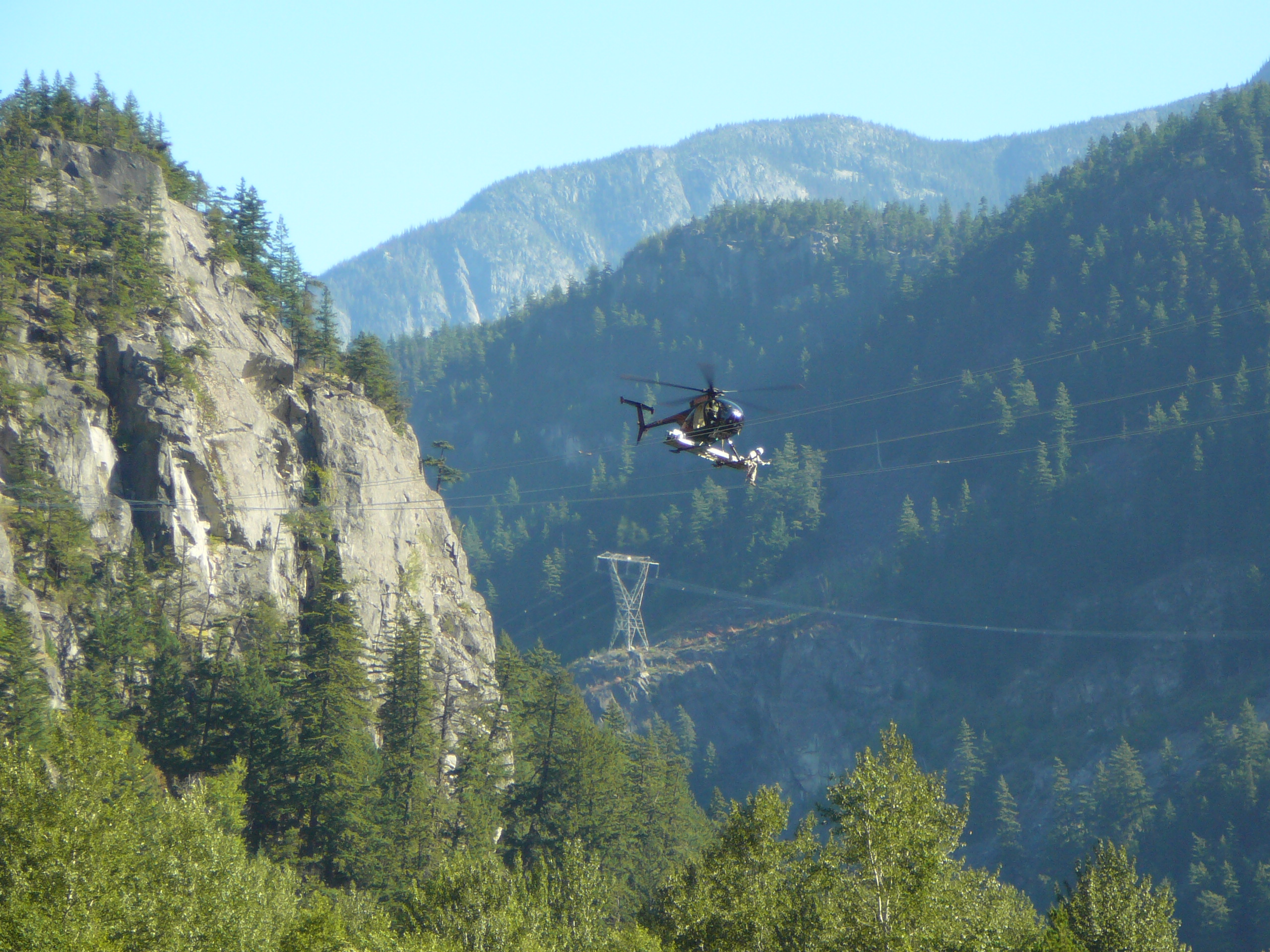 A helicopter is flying through mountains with electric lines nearby.